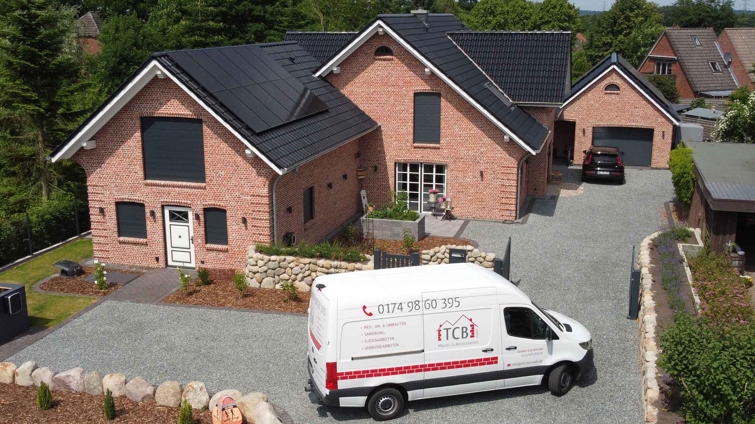 Luftaufnahme eines Backsteinhauses mit Solaranlage und einem TCB Maurer- & Betonarbeiten Firmenfahrzeug davor