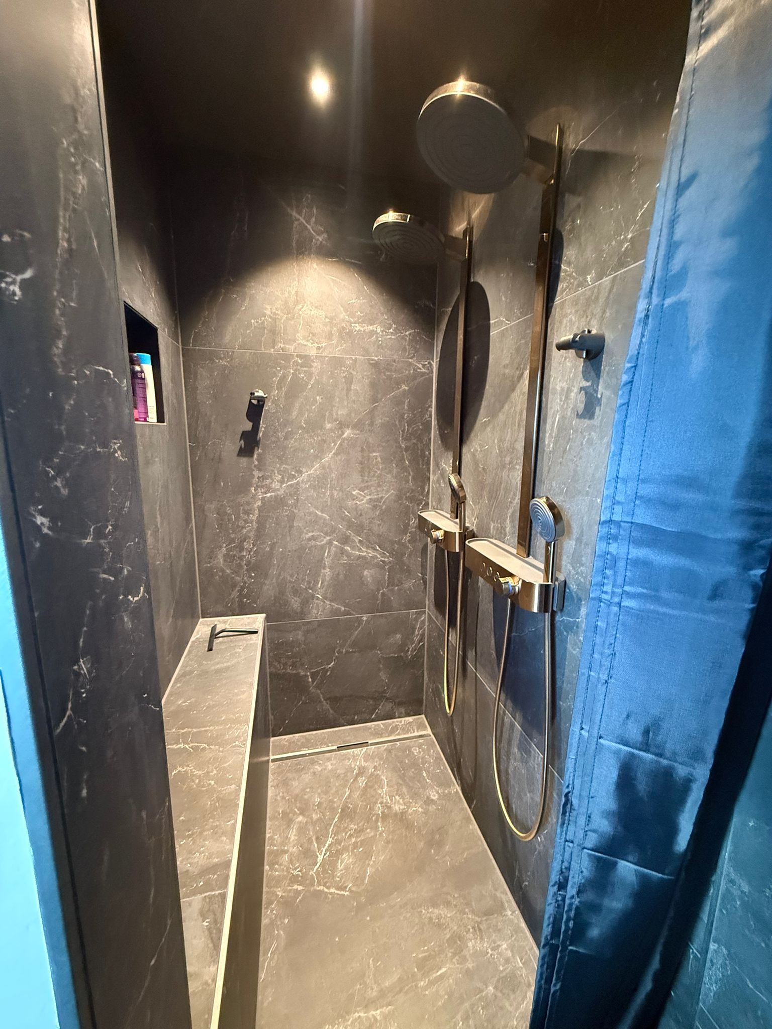 Moderne Dusche mit dunklen Marmorplatten, Regenduschkopf, Handbrause und blauem Duschvorhang
